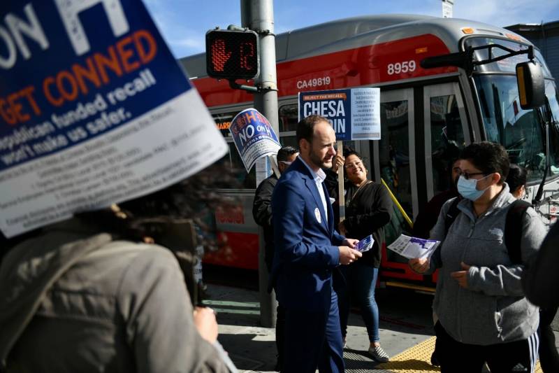 A man handing out flyers in front of a bus