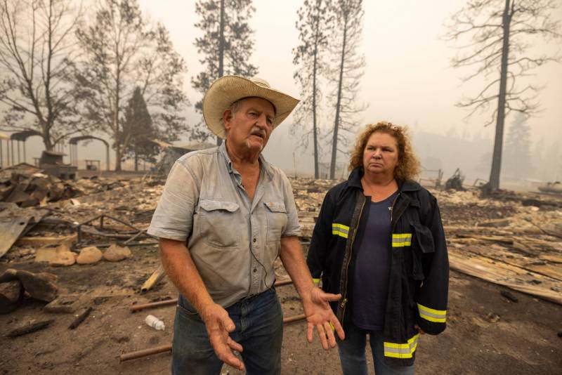 A man wearing a cowboy hat is talking. A woman in a fire personnel jacket stands next to him