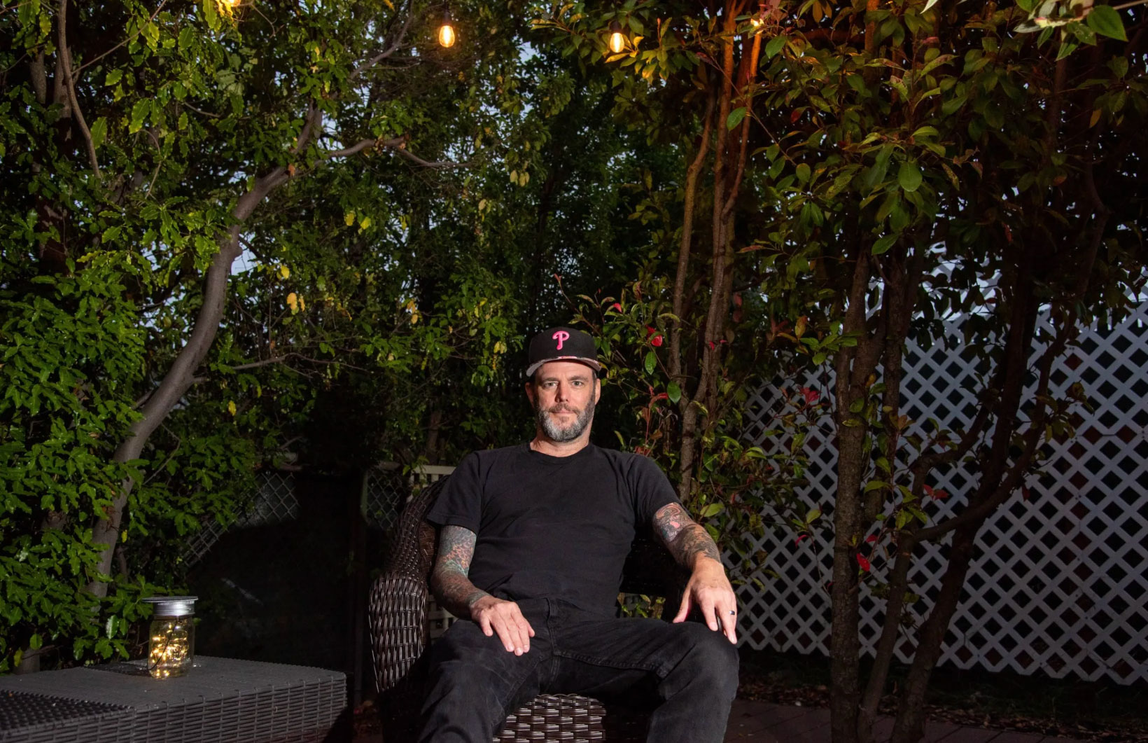 Bearded man sitting in a chair on a patio at night lighted by overhead string of lights