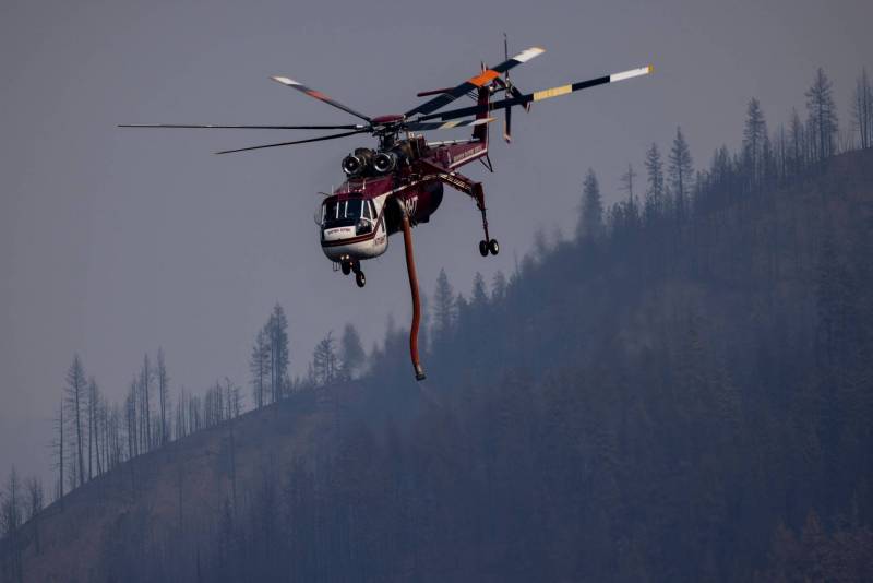 A helicopter flying over hills with burned trees