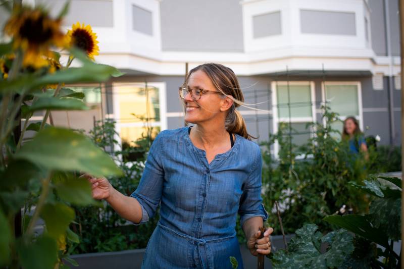 A woman wearing glasses and a blue shirt stand in the middle of a garden.