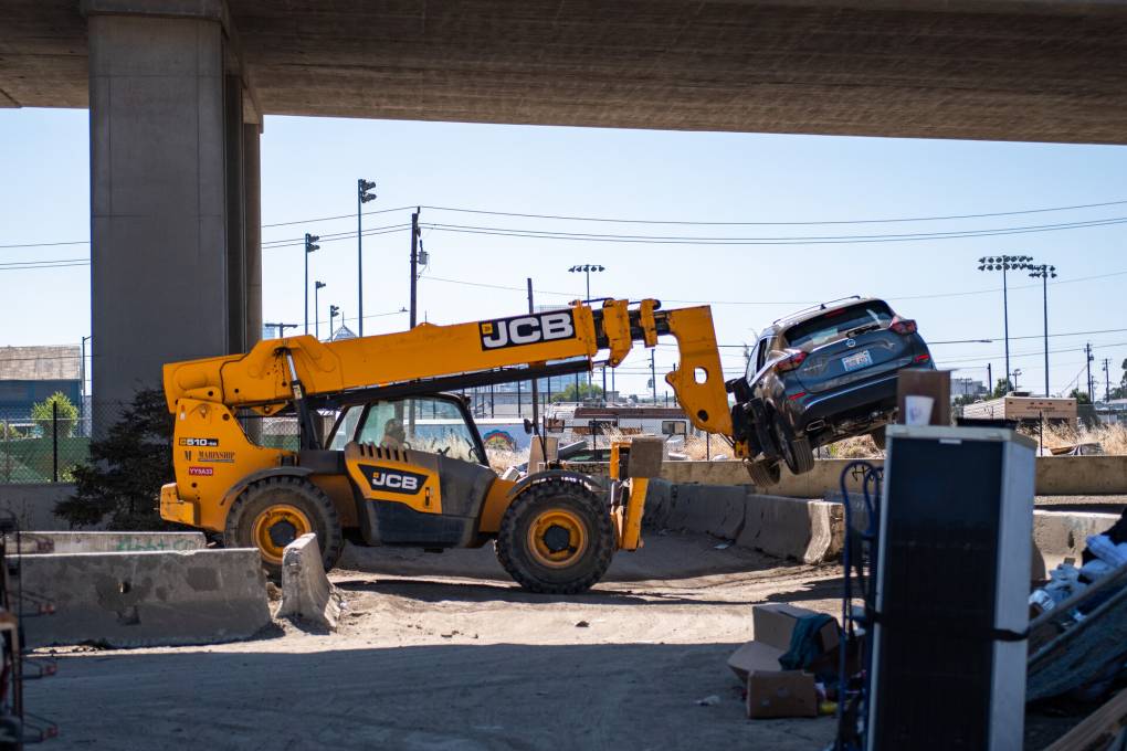 an orange construction vehicle removes a car from a homeless encampment