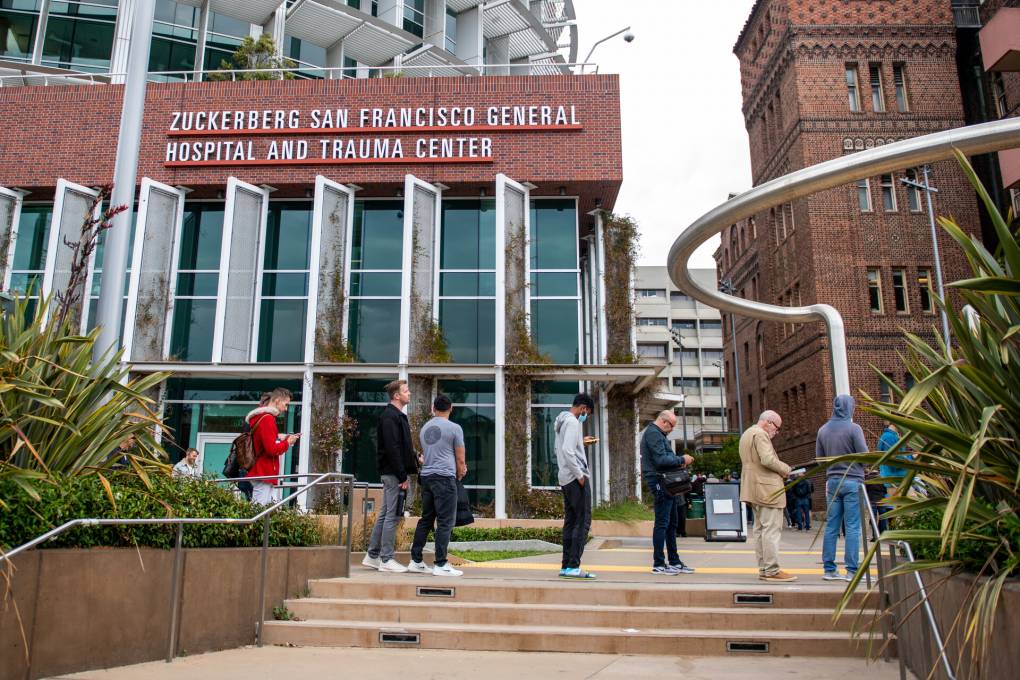A long line of men wait in line in front of a Zuckerberg San Francisco General Hospital