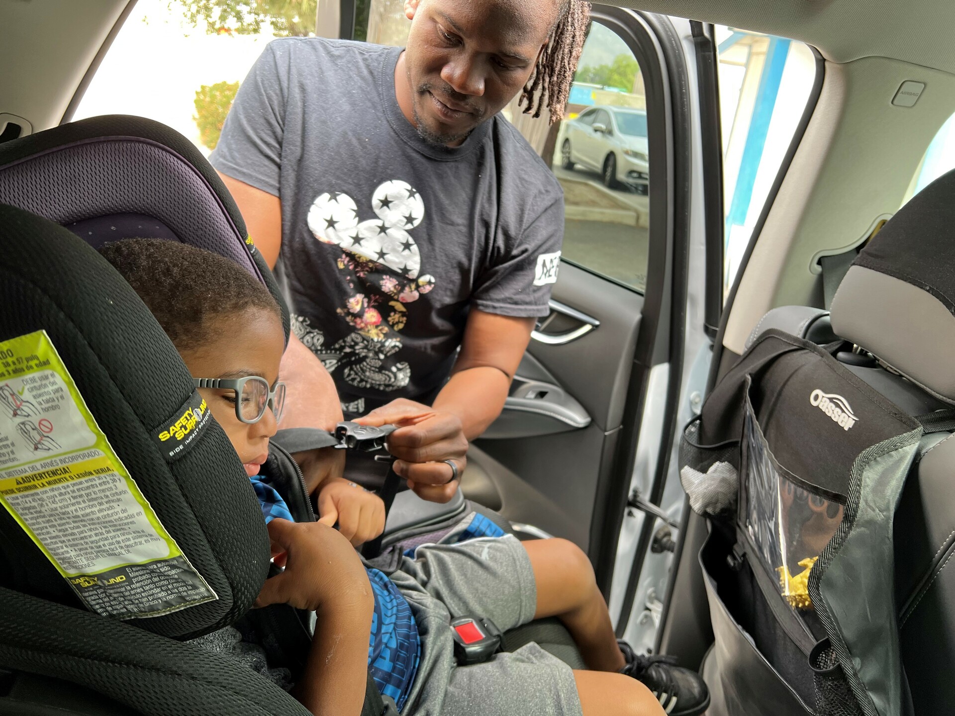 A man is putting a child into a car seat.