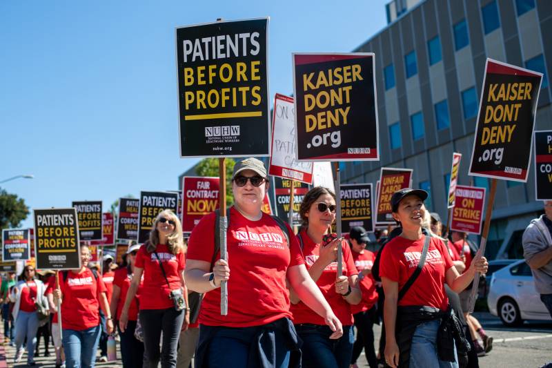 people in red shirts carrying signs that read "patients over profits"