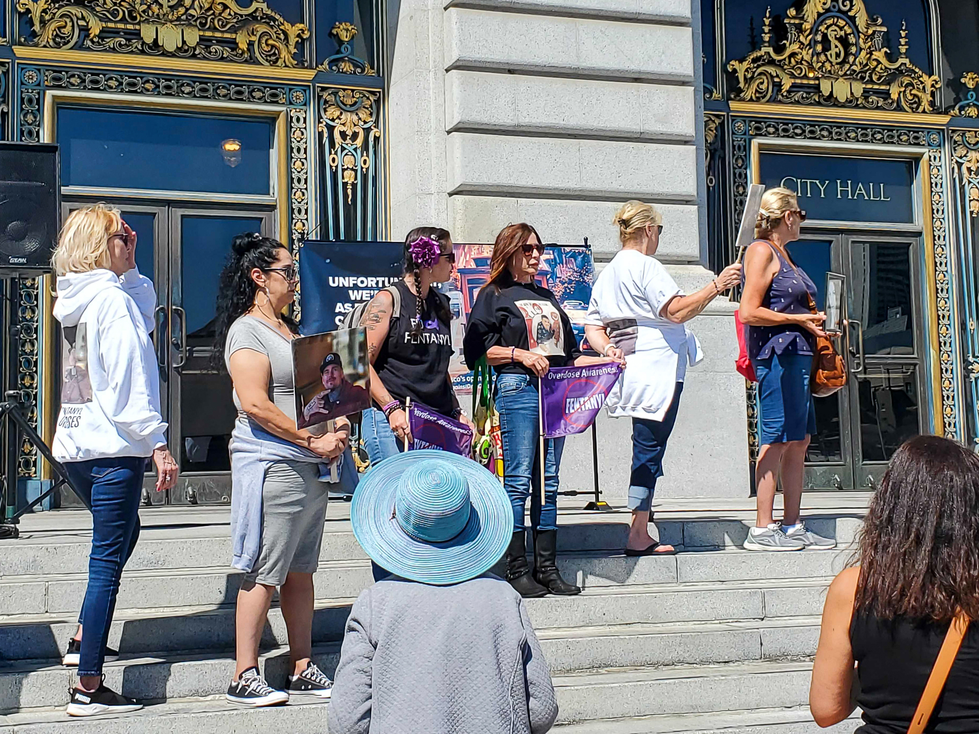 a line of women prepare to speak on the steps of San Francisco City Hall at a rally against fentanyl deaths