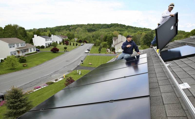 two men install solar panels on a roof