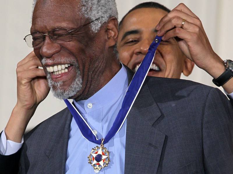 Former President Barack Obama puts a medal around the neck of an older Black man, former Boston Celtics captain Bill Russell, as both smile
