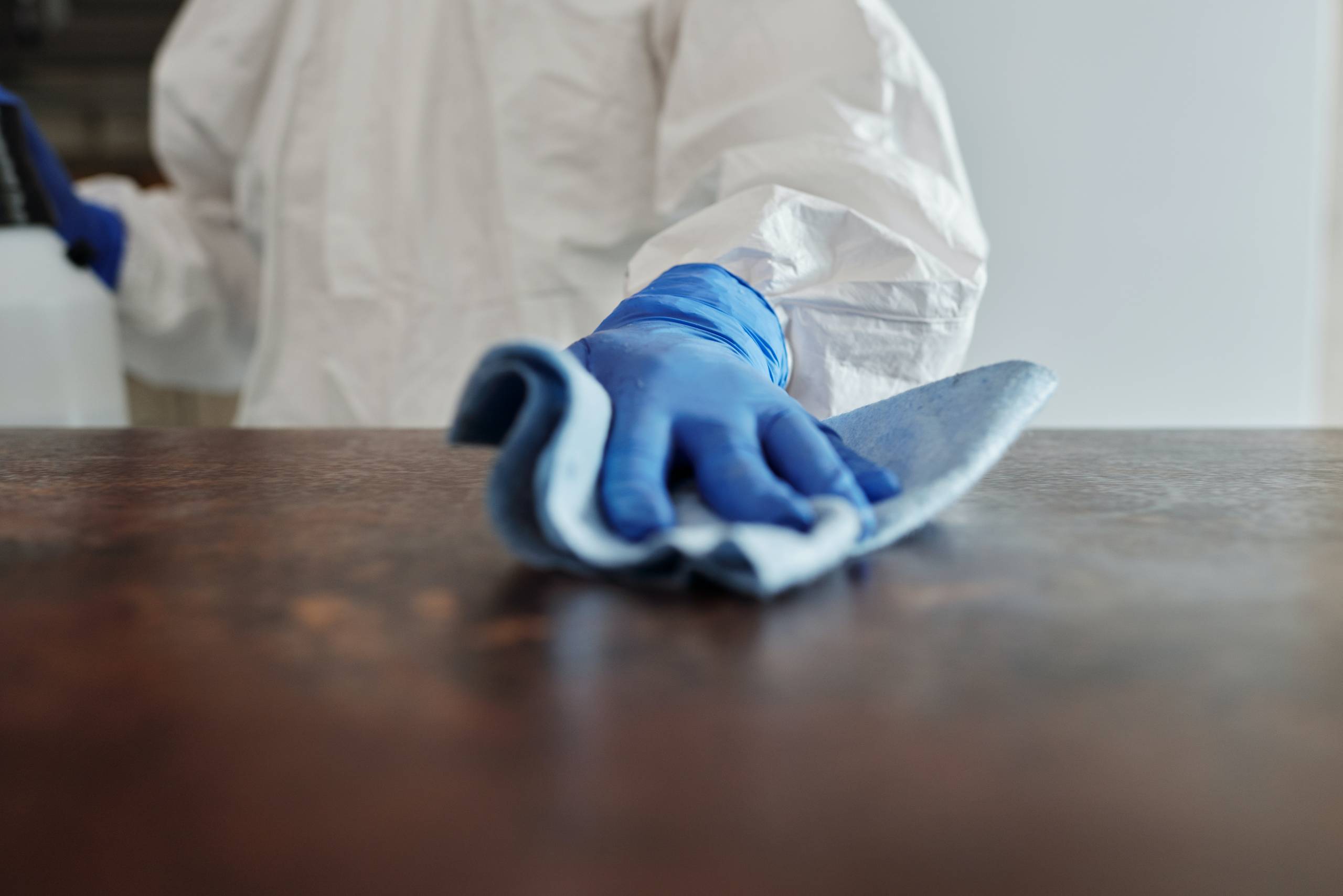 A person wearing personal protective equipment wipes down a table indoors.