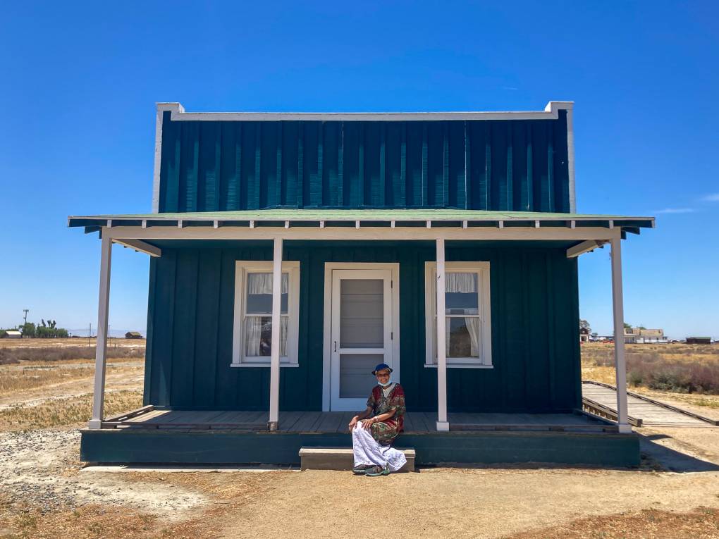 a woman sits in front of a blue building in a desert