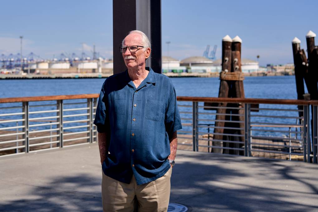 A man wearing a blue shirt and glasses stands outside on a dock.