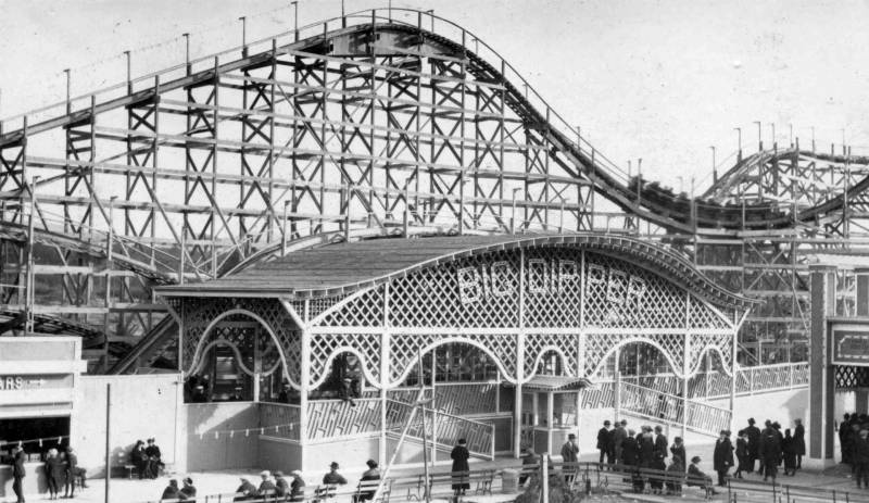 Black and white photo of people lining up to ride a roller coaster. A wooden structure at the entrance to the ride has the words BIG DIPPER across it.