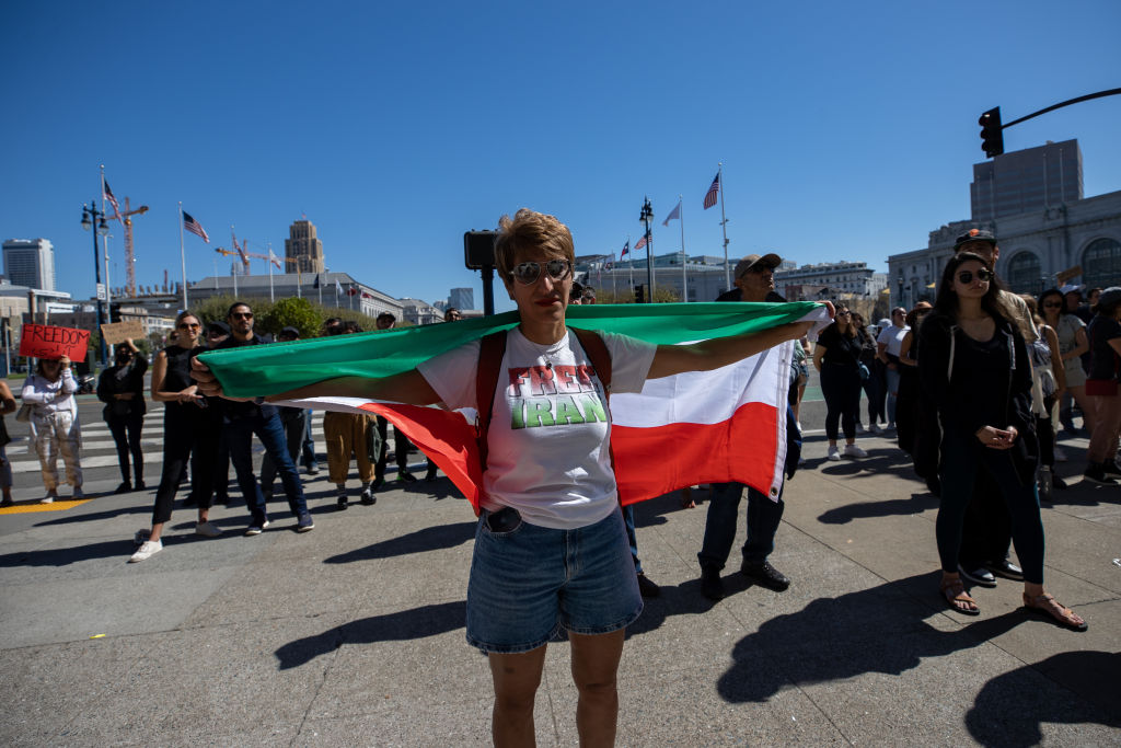 a person draped in an Iranian flag stands outside San Francisco City Hall