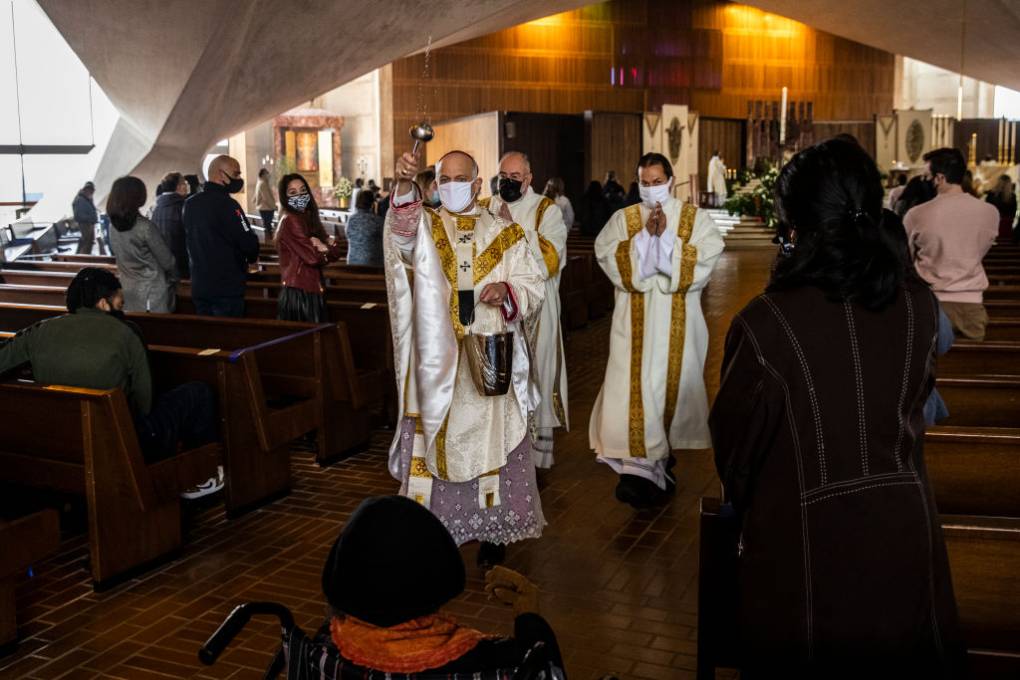 a scene inside a church with the archbishop of San Francisco sprinkling holy water on church attendees