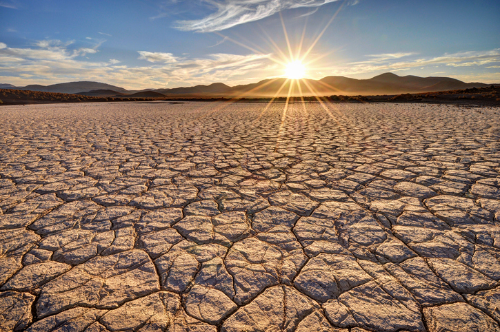 A cracked dry lake bed as the sun sets over distant hills