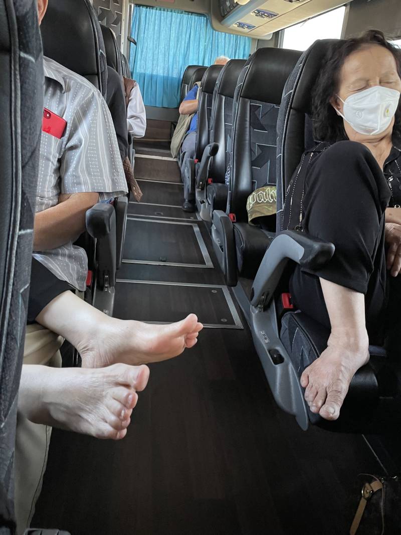 Bare feet are seen coming from a seat while people sit on a bus.