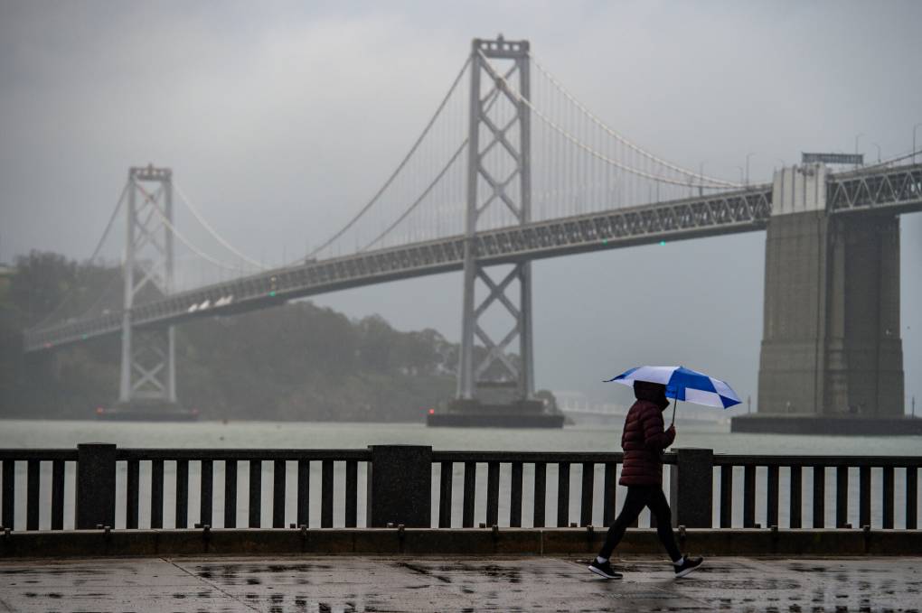 a foggy shot of the Bay Bridge with a person walking with an umbrella