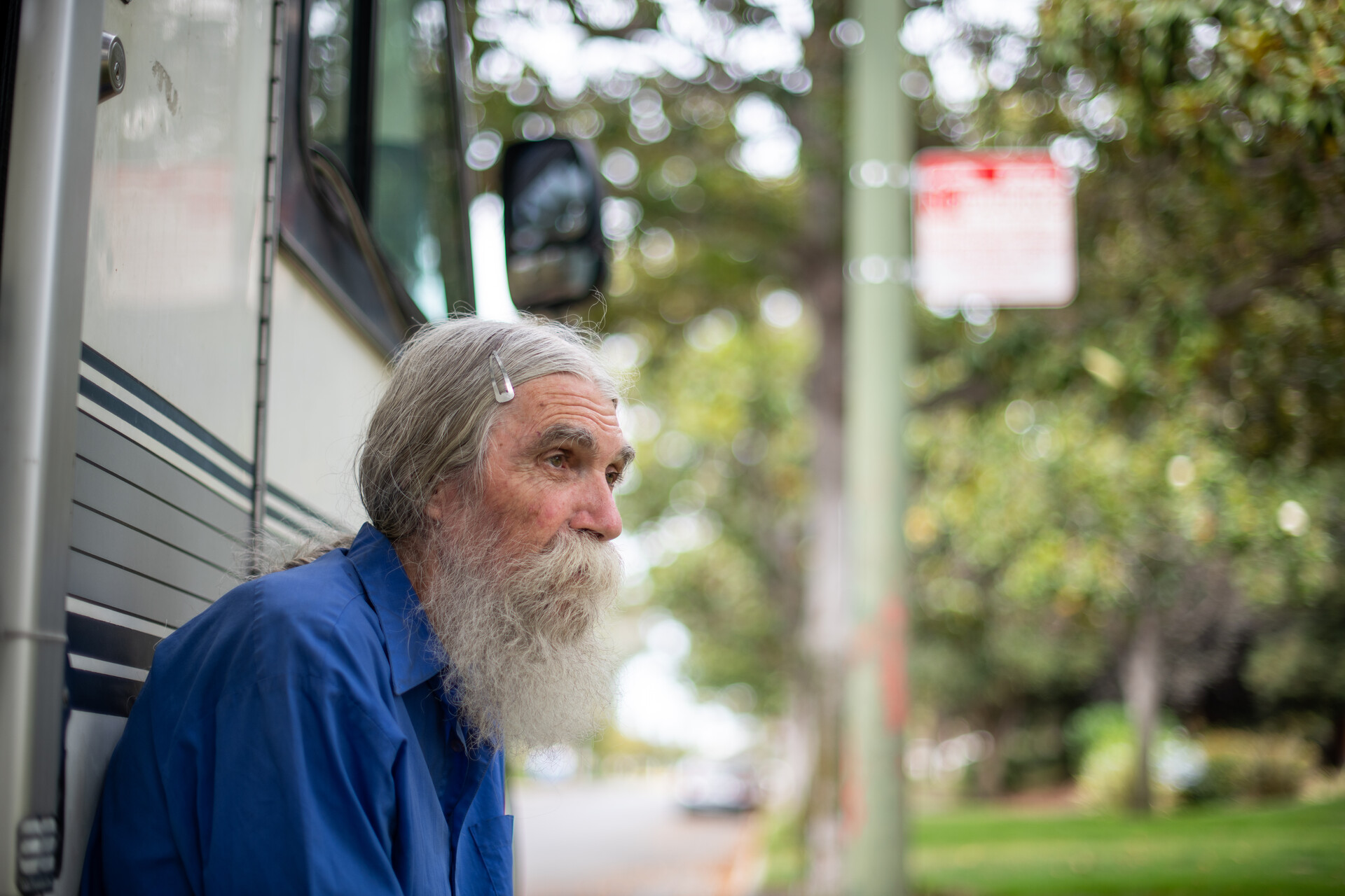 Close up photo of elderly man wearing blue shirt with large gray beard with exterior wall of RV behind him