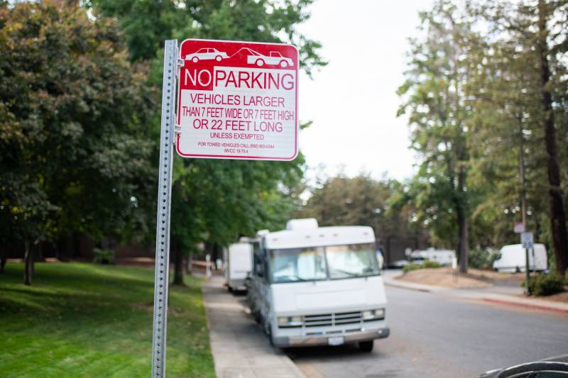 a red and white 'no parking' sign is seen on a street where an RV is parked