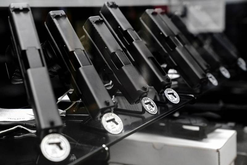 The image shows a row of the flat barrels of black pistols, as viewed from above. The are displayed on a rack.