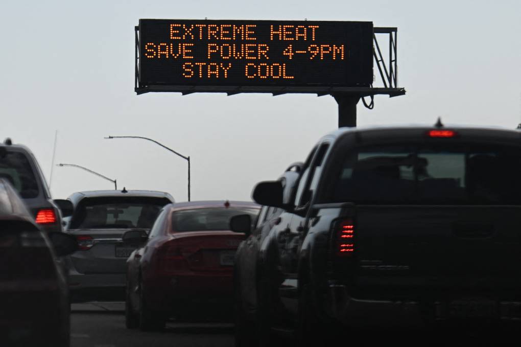 Cars in traffic with a sign above saying 'Extreme Heat Save Power 4-9pm Stay Cool'