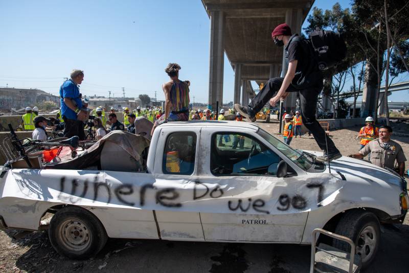 People standing on a car that is spray-painted saying: 'where do we go?'