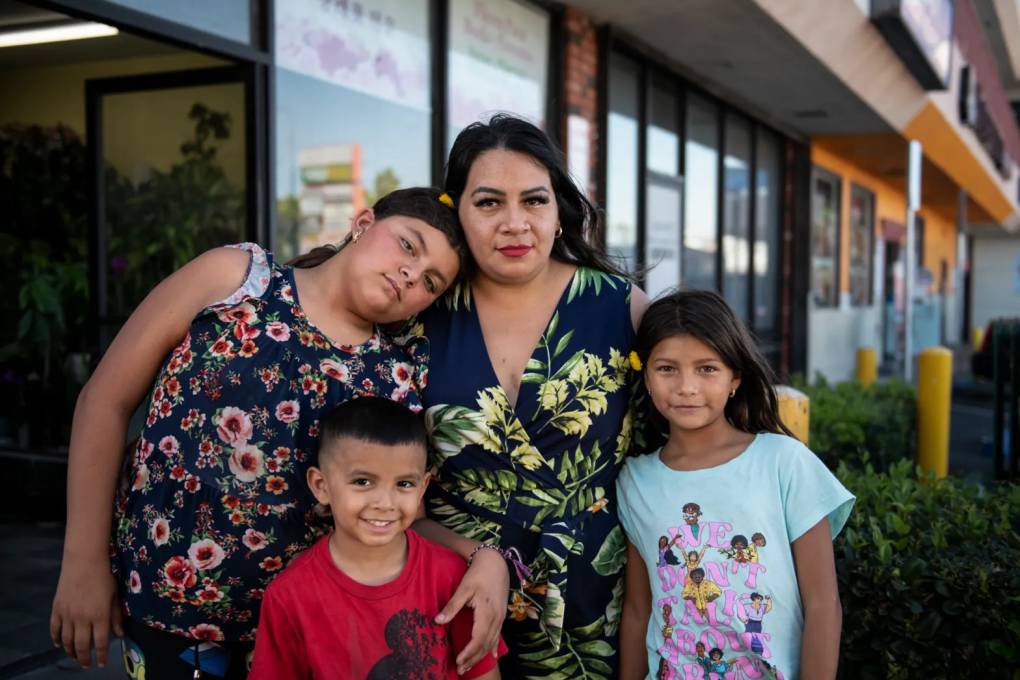 A Latina woman stands with three children of varying ages as they all smile for the camera.