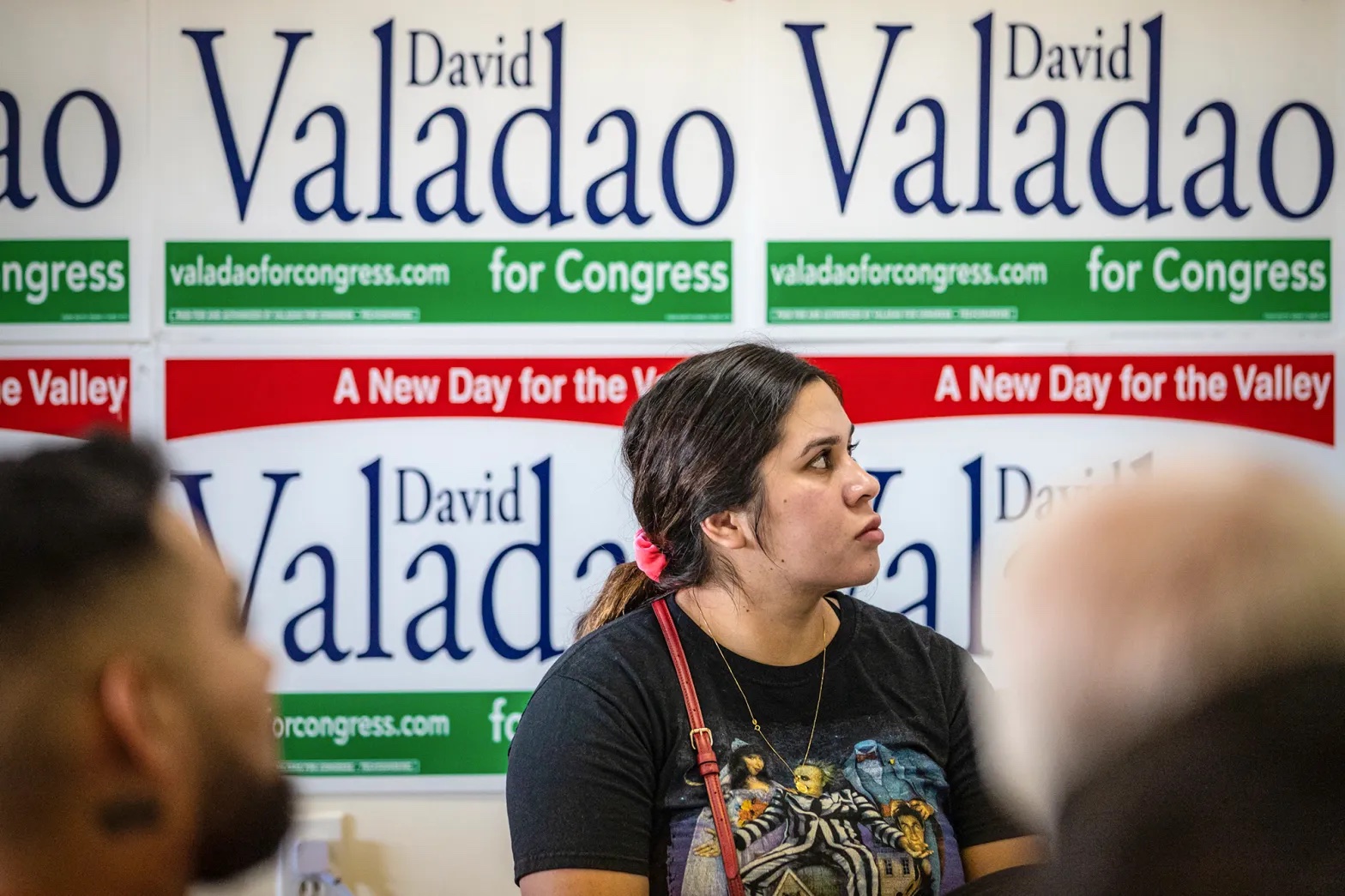 A young Latina woman looks on with a poster behind her that says "David Valadao for Congress"