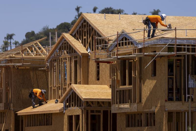 newly framed homes without any siding yet on them are shown with two construction workers climbing on them