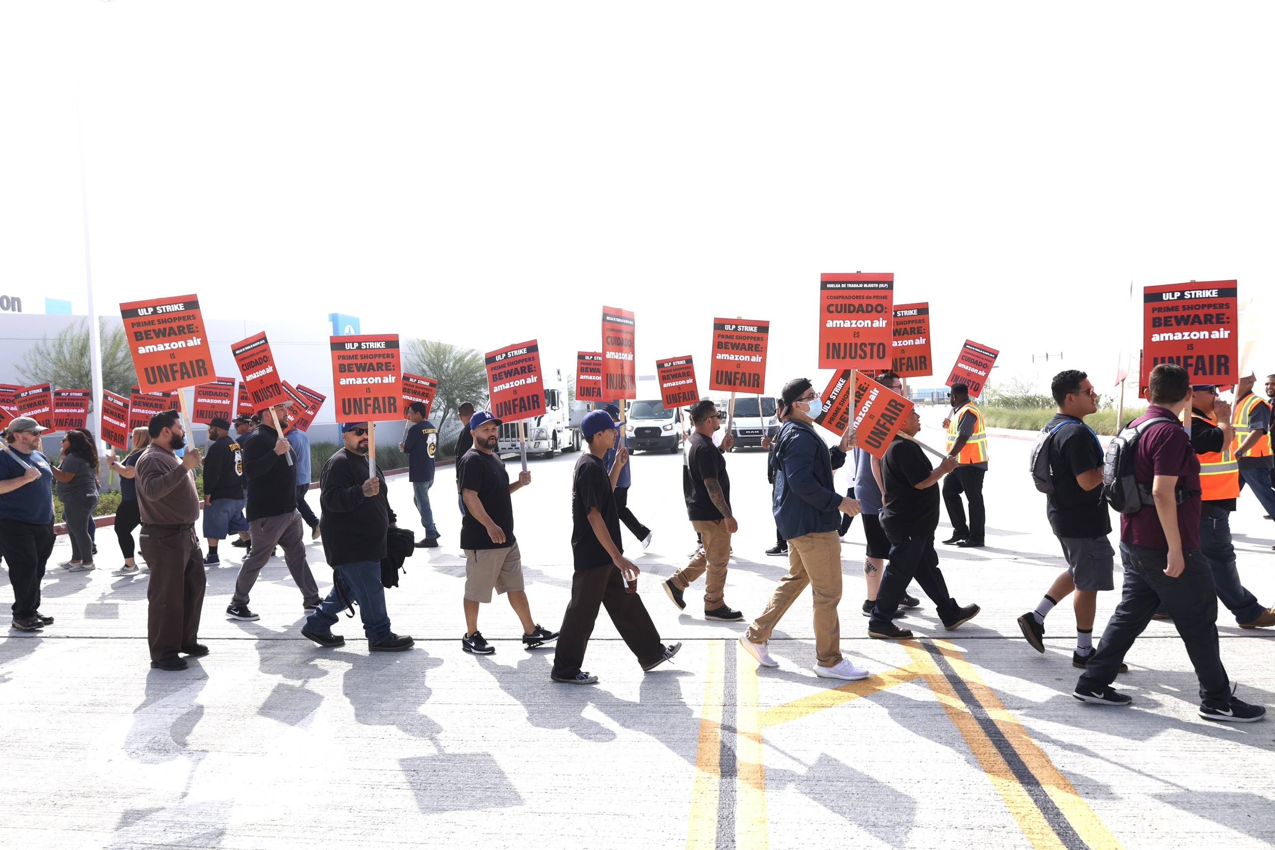 Dozens of strikers march with signs on a tarmac.
