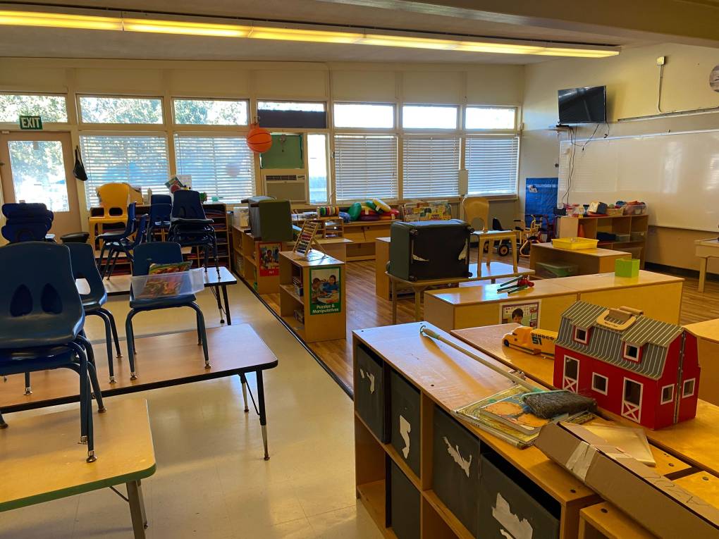An empty preschool classroom with chairs on desks.