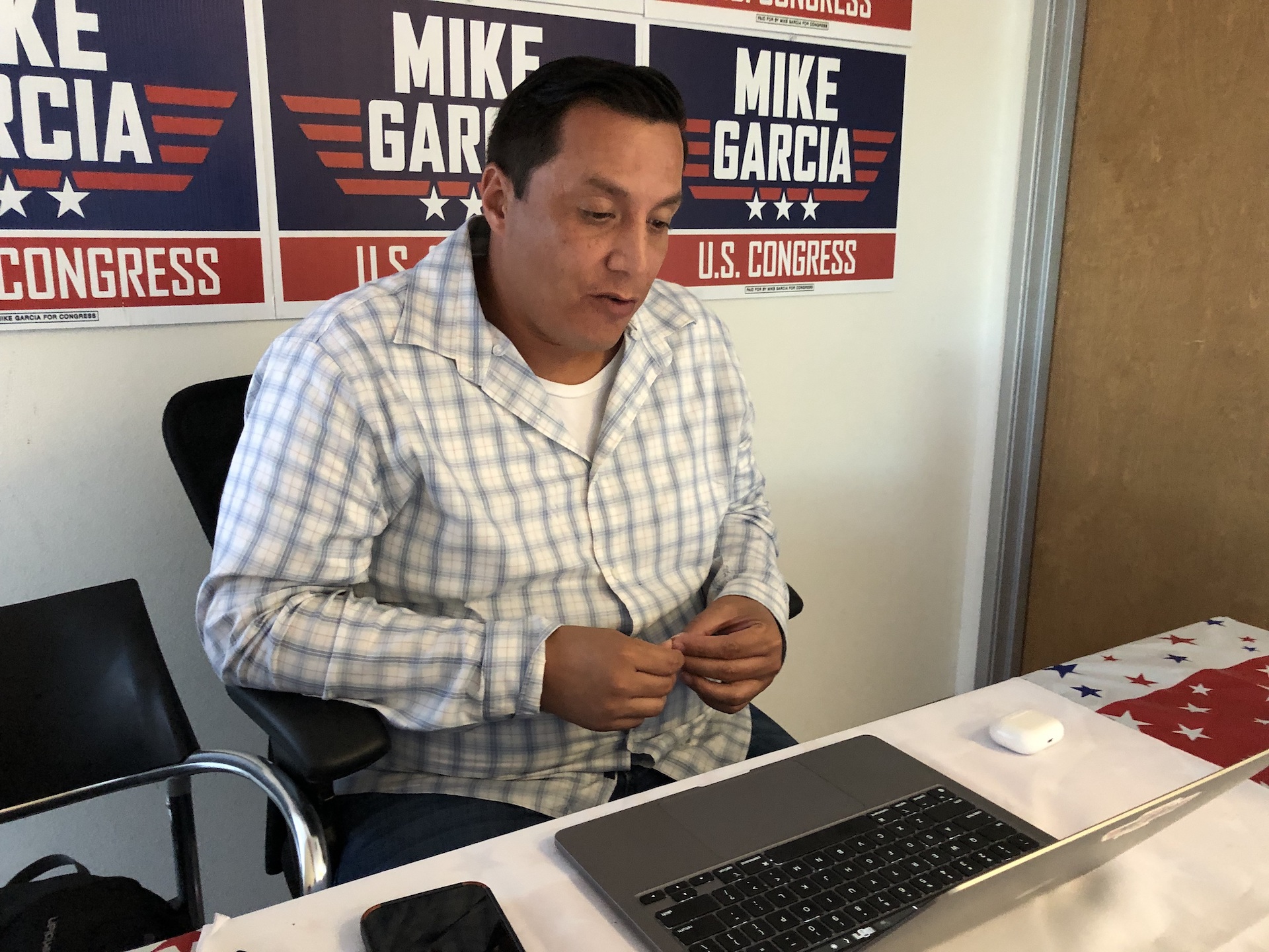 A man sits at a desk in front of a computer, with signs for Mike Garcia posted behind him.