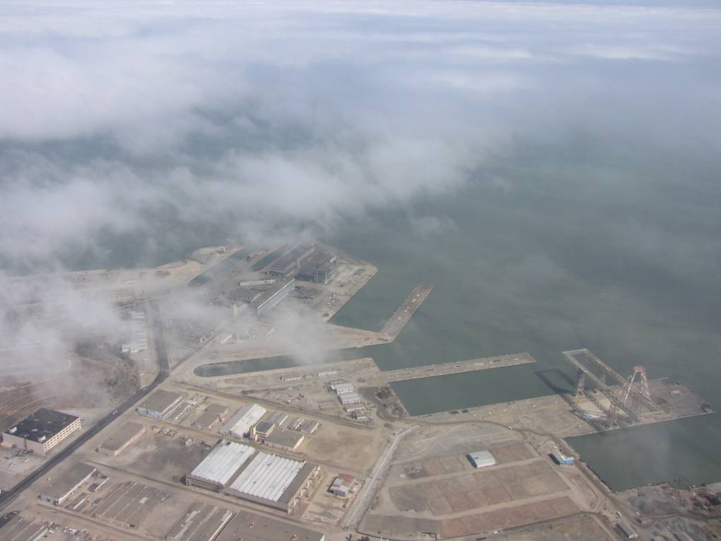 A view from the air of a naval shipyard with clouds partially covering the photo.