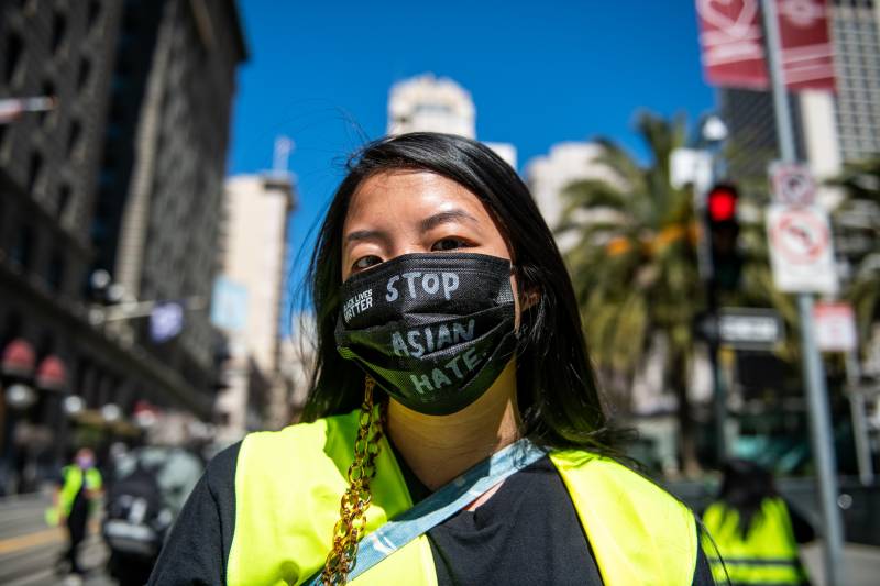 a young Asian American woman wears a black mask that reads 'stop Asian hate'