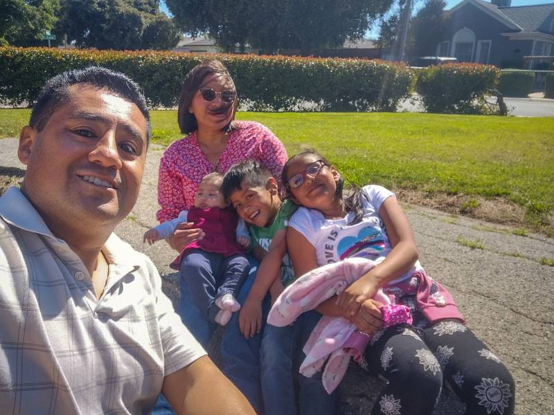 a Latinx family posing in a park, with a dad, mom and three young kids