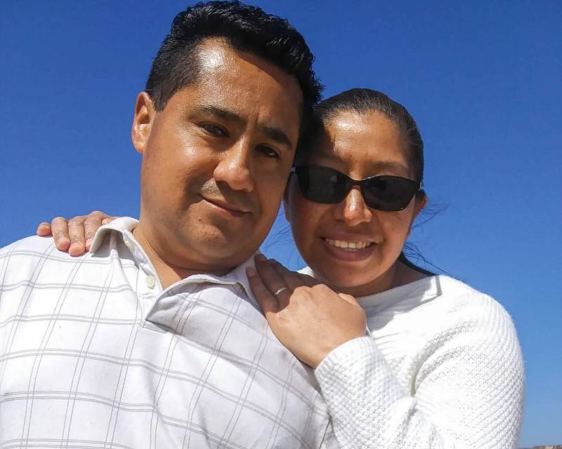 a young Latinx couple, a man and a woman, in white shirts, smiling in front of a blue sky