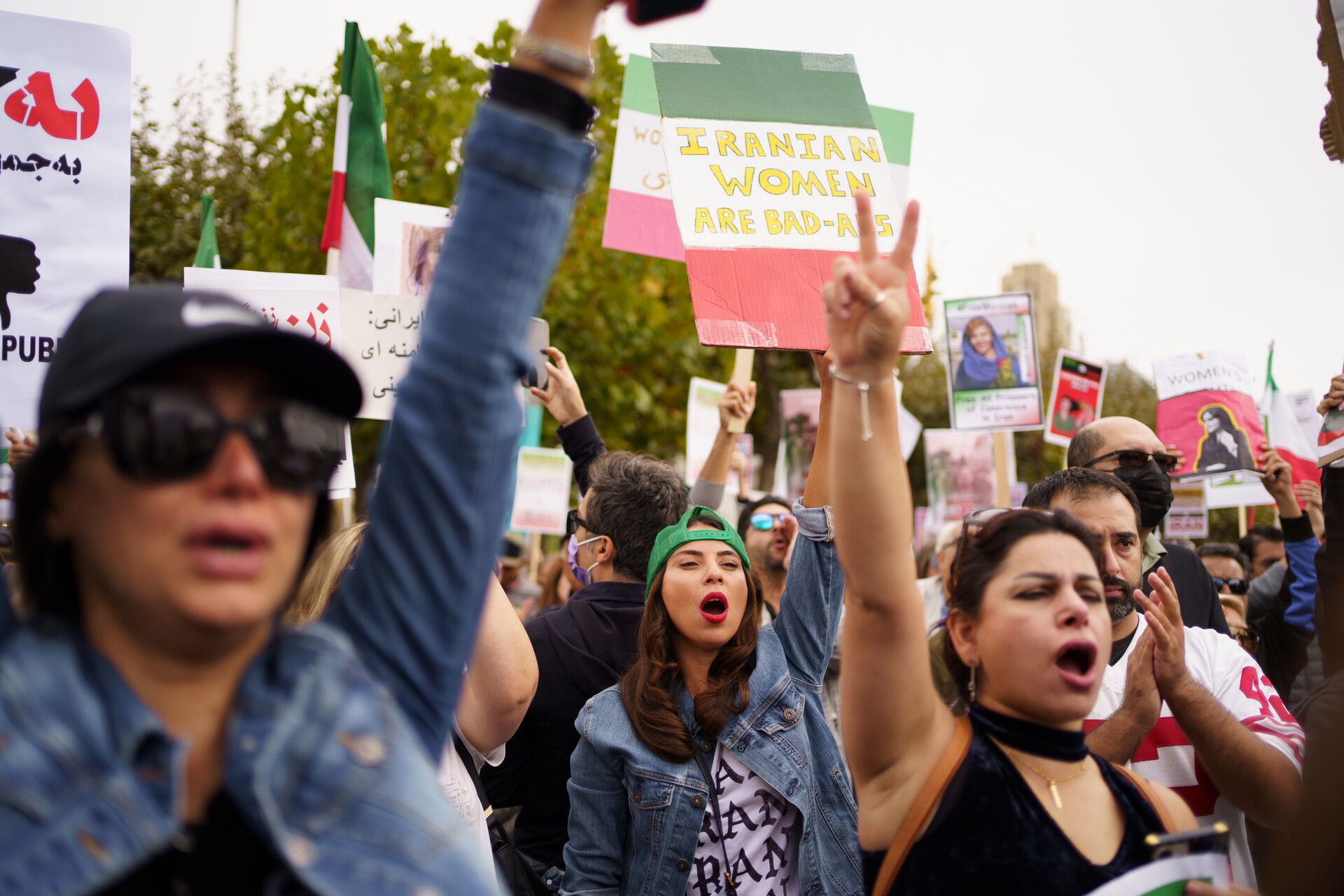 Several women in a crowd raising their hands and holding signs and flags in a large crowd outside.