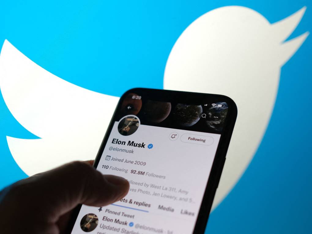 A hand holding a smartphone showing Elon Musks Twitter account.