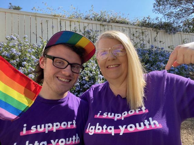 a young man and his mom smile for a portrait wearing purple shirts that read 'I support LGBTQ youth'
