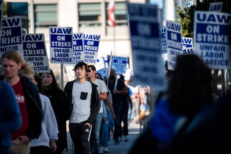 people march and hold signs reading 'UAW on strike unfair labor practice'