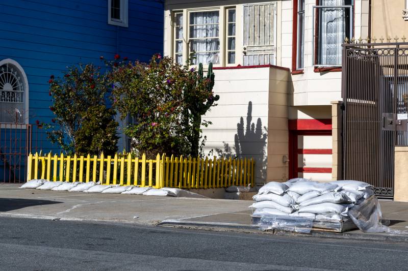 A house with sandbags in front of the yellow fence and on the sidewalk.