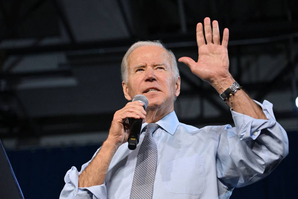 Biden stands holding a microphone with one hand held up next to him