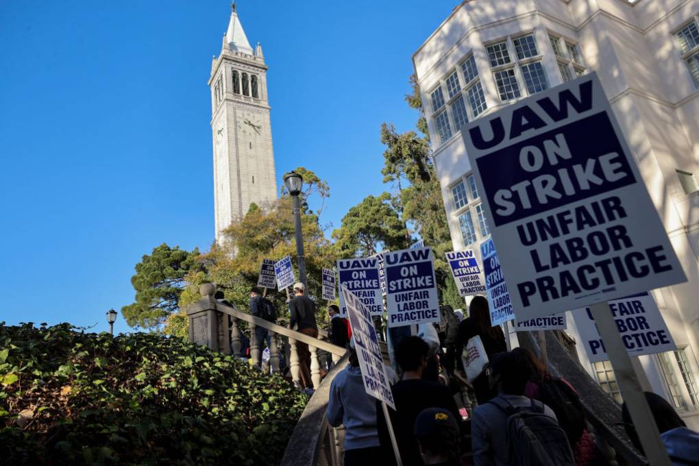 a sign that reads 'UAW On Strike, Unfair Labor Practices' is held during a strike in front of UC Berkeley's campanile tower