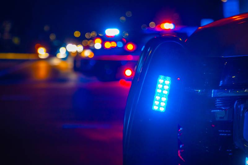Blue police light flashes on a generic crime scene at night in an urban area.