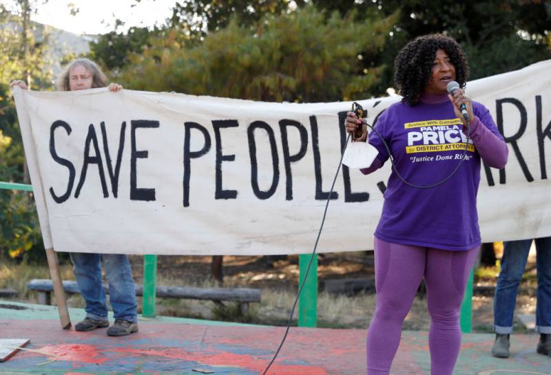 A woman speaks into a microphone, standing in front of a banner that reads: 'Save People's Park.'