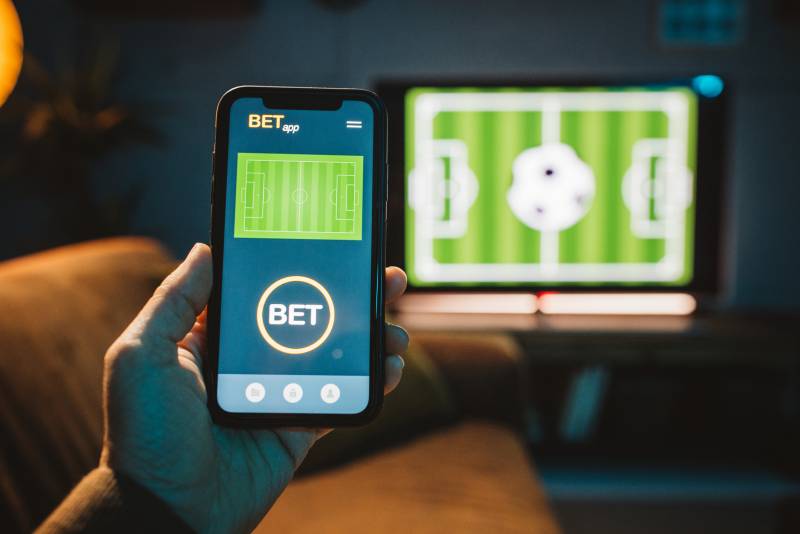Close up of men's hand using smart phone for sports betting.