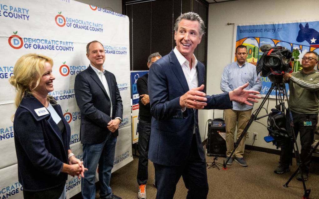 Gov. Gavin Newsom gestures while speaking in a room, with officials standing behind him.