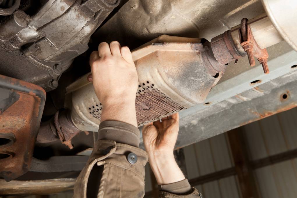 A pair of hands removing a catalytic converter.