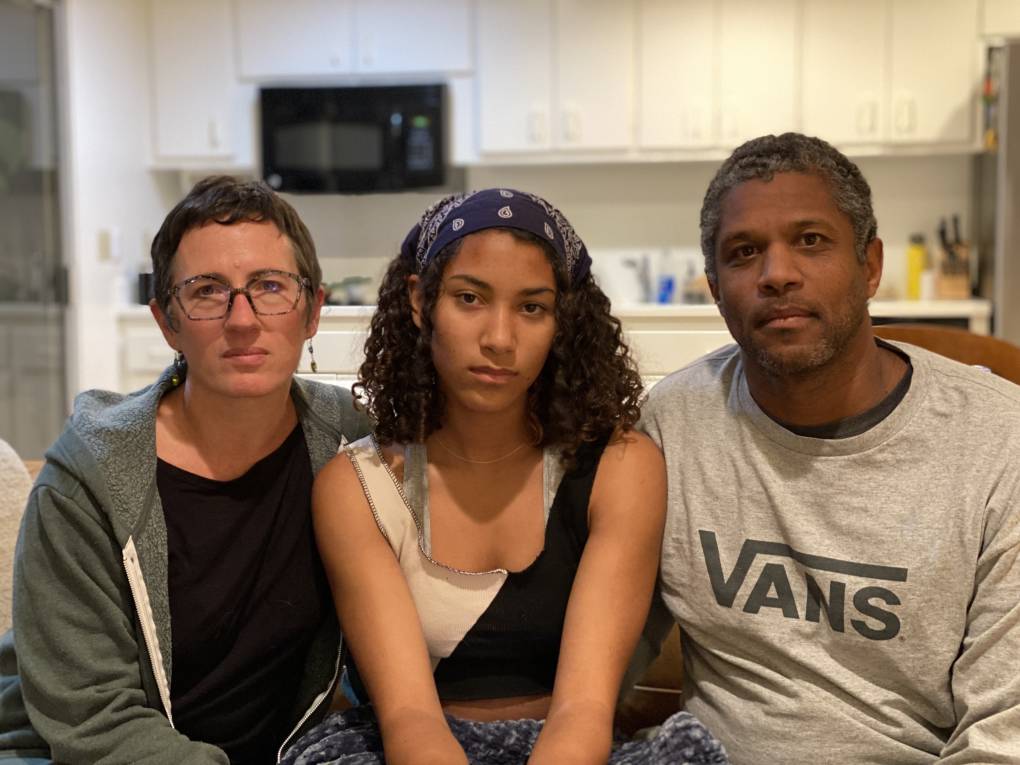 a young woman with curly hair sits between her parents in their kitchen