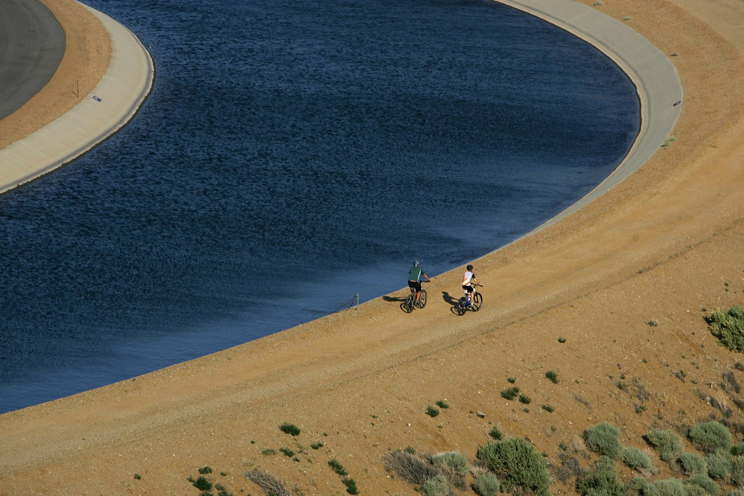 Two cyclists ride by an irrigation canal.
